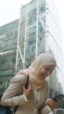 Vertikales-Video-Einer-Muslimischen-Geschäftsfrau,-Die-Gute-Nachrichten-Auf-Dem-Mobiltelefon-Feiert-Und-Vor-Dem-Büro-In-Der-Stadt-Steht